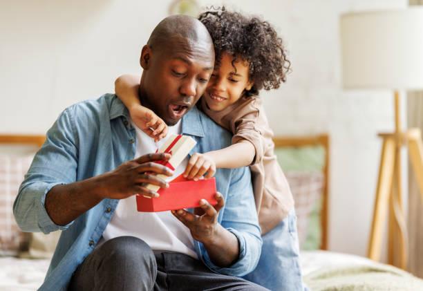 Image of a child hugging his dad while he opens a gift. Kids spend less on father's day than mother's day