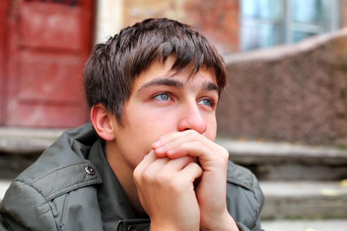 A sad-looking young man sits on the steps outside some flats