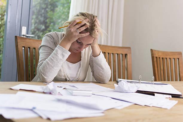 Image of woman with her head in her hands looks at bills in front of her