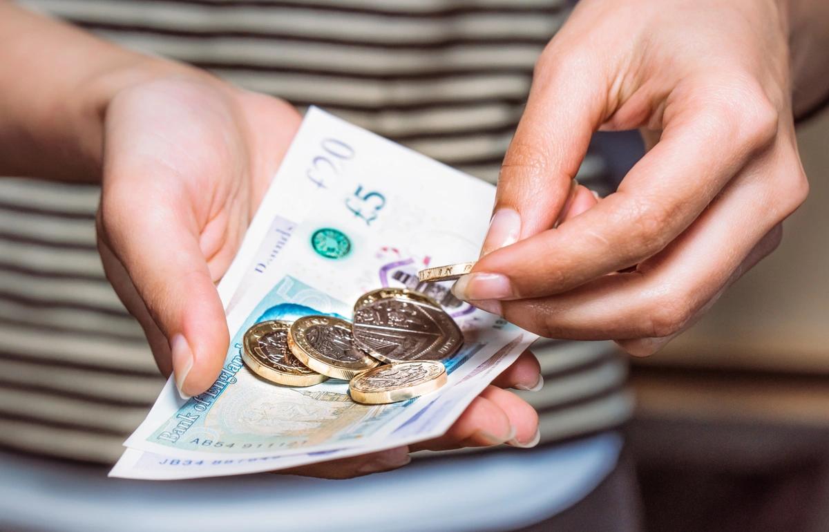 A close-up of a woman's hands holding banknotes and coins