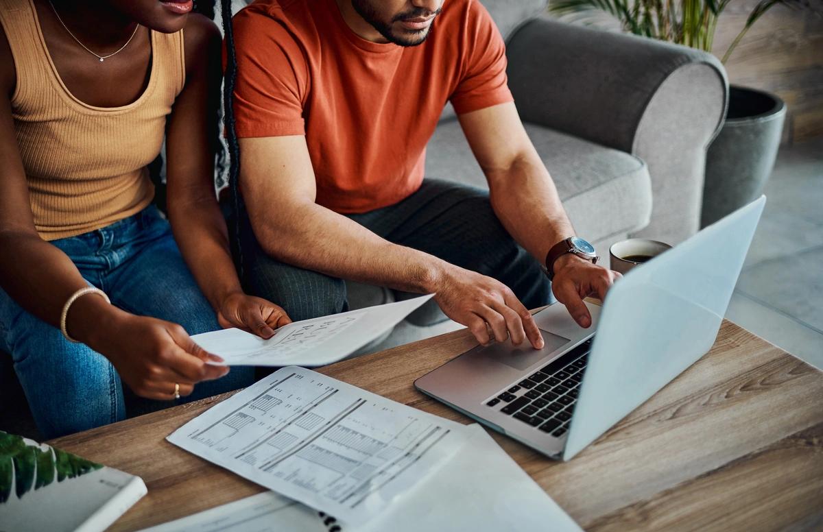 A close up of a couple sitting at a laptop and ging through their bills