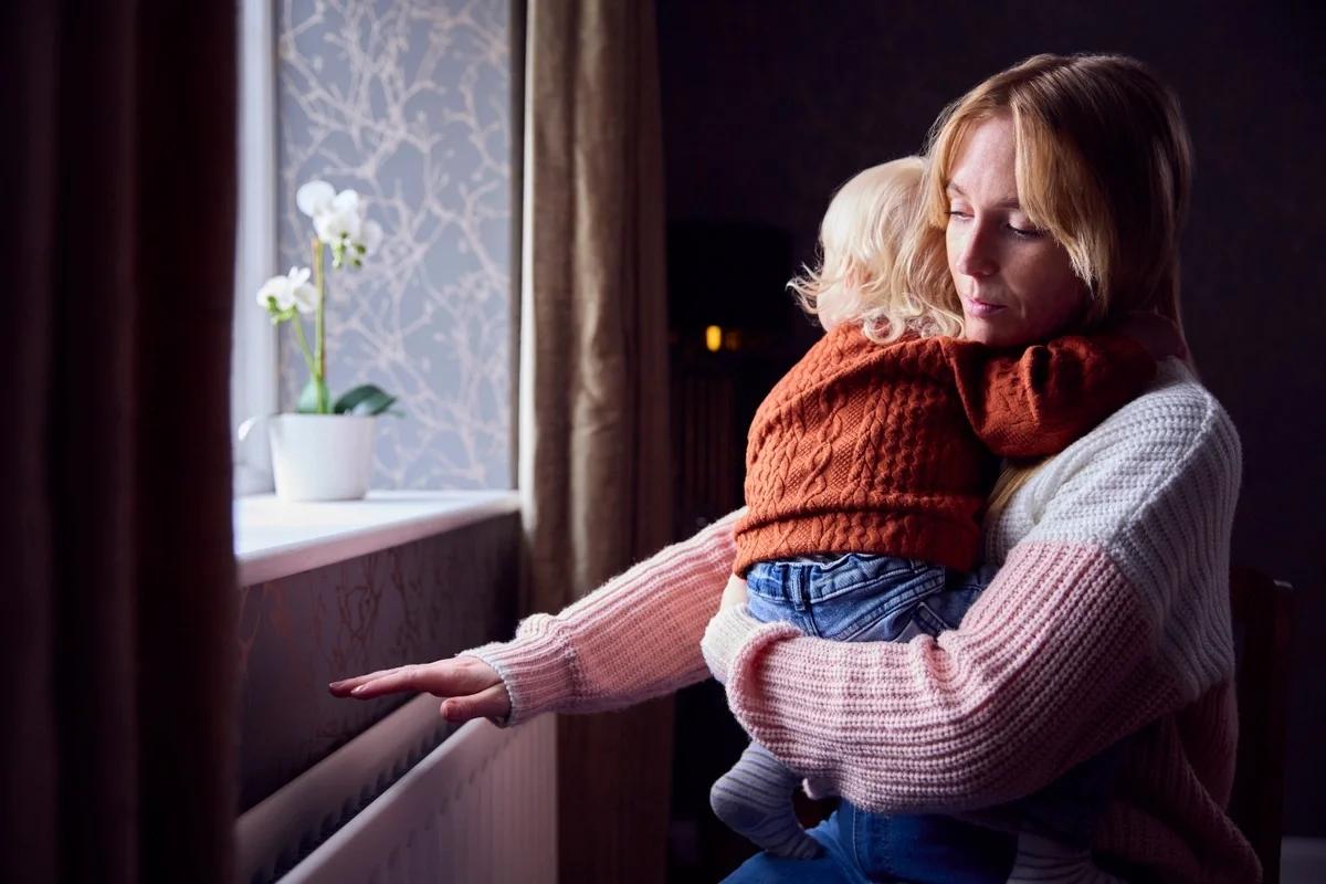 A mum holding her young son tries to keep warm by the radiator