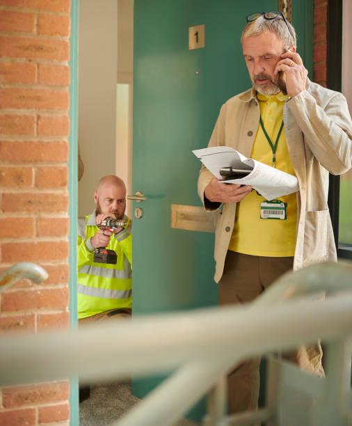 Image of a man outside a house on the phone while someone changes the locks. Home arrears are falling. But help is still here if you’re struggling to keep up with mortgage repayments