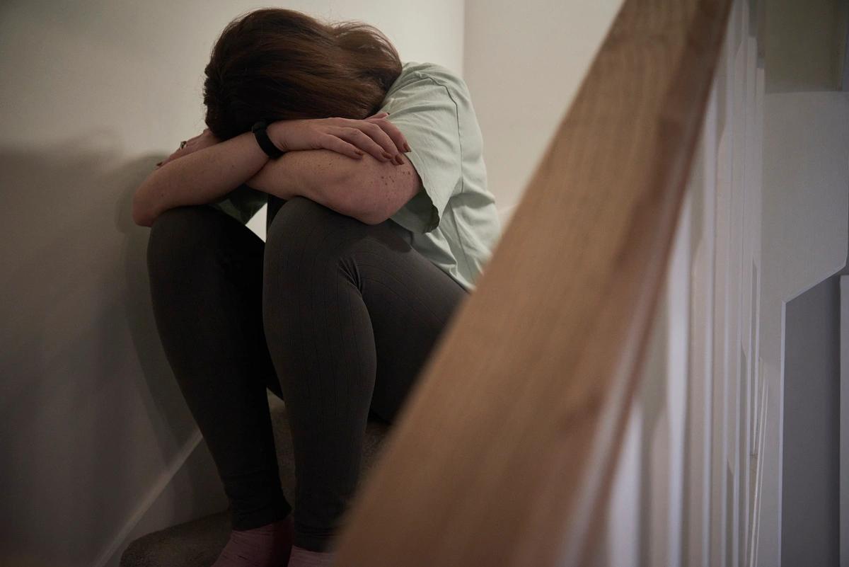 A woman sits on the stairs with her head in her hands