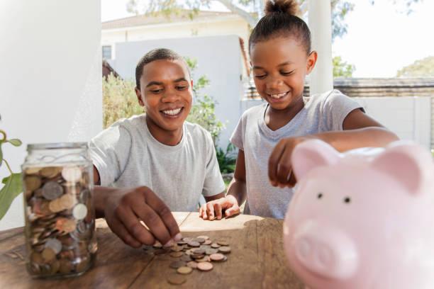 teenage boy and young girl counting out money from a piggy bank and jar