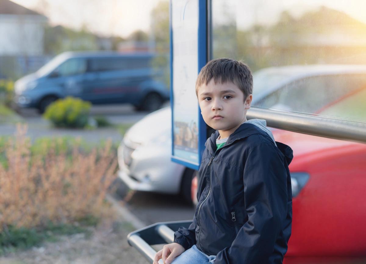 A serious young boy sitting at a bus stop