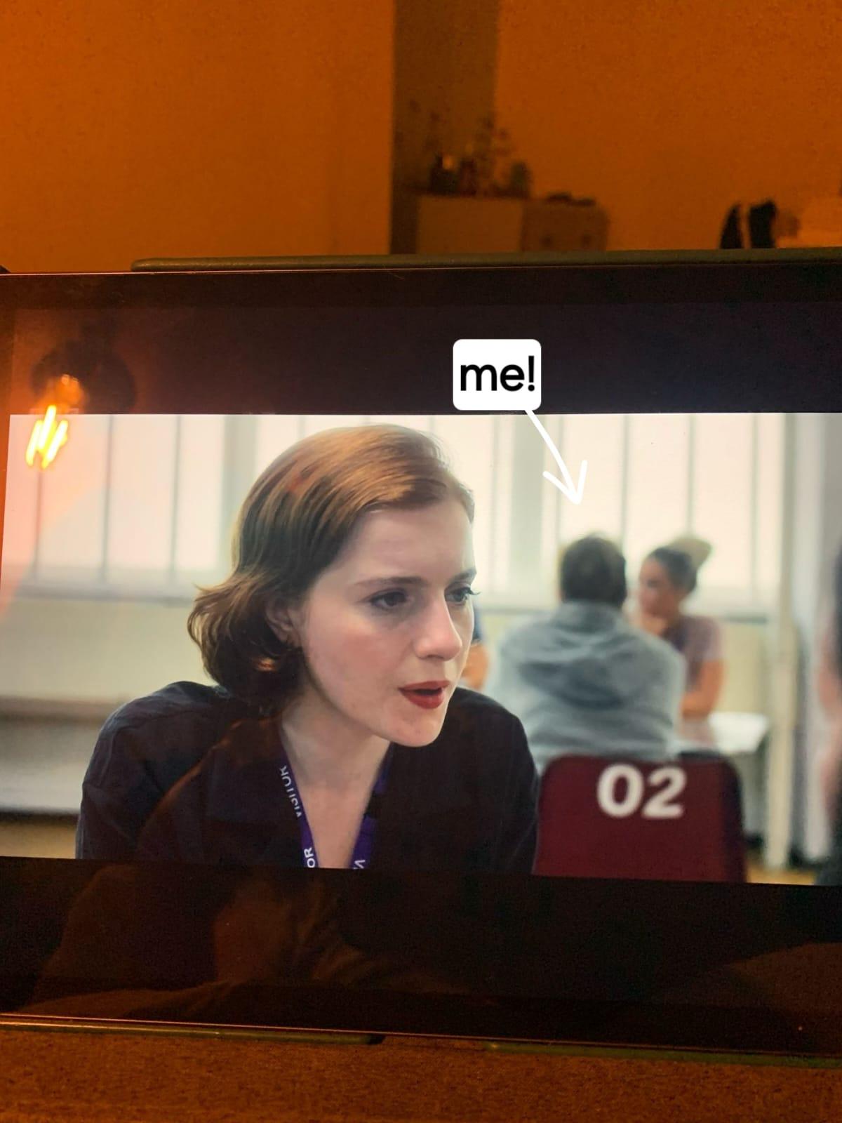 A photo of a television screen with an arrow and the word 'me' pointing at an extra in the background