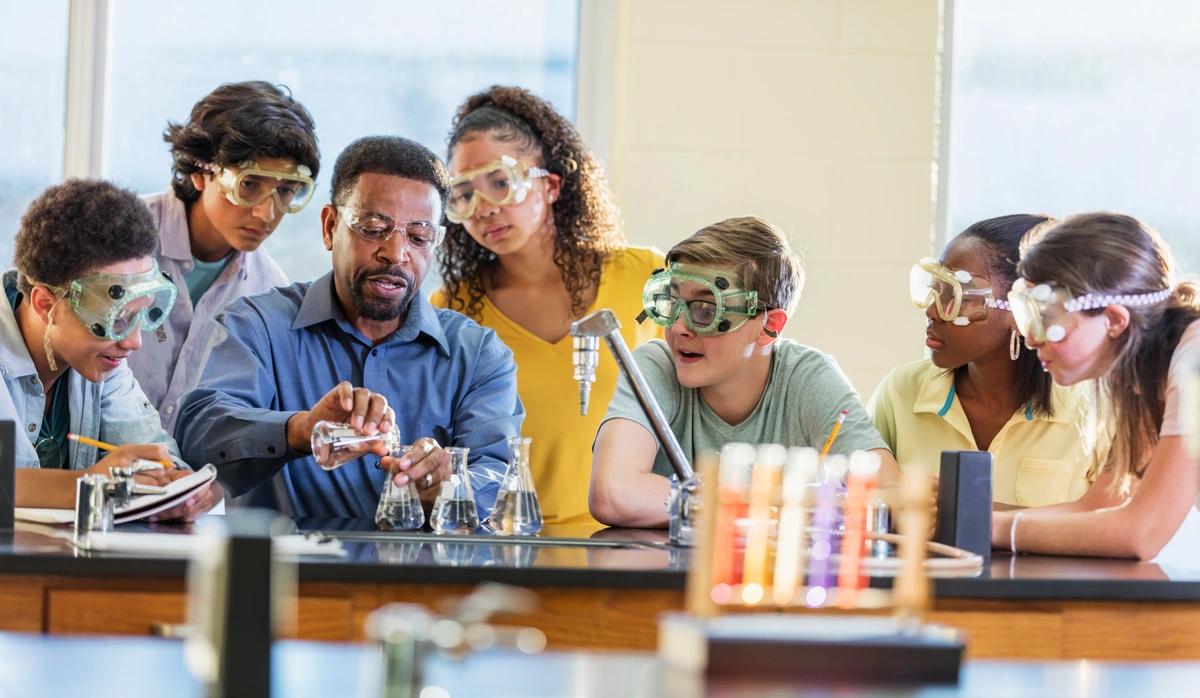 A science teacher carrying out an experiment surrounded by children in protective eye goggles