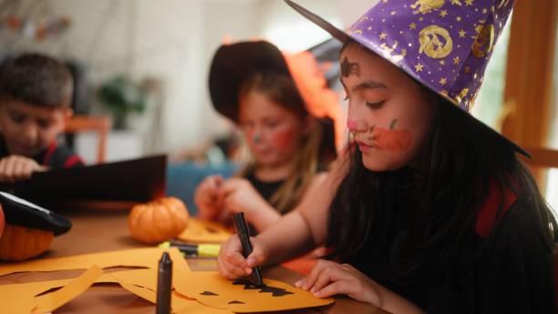 Image of a little girl dressed up as a witch making a scary pumpkin out of cardboard