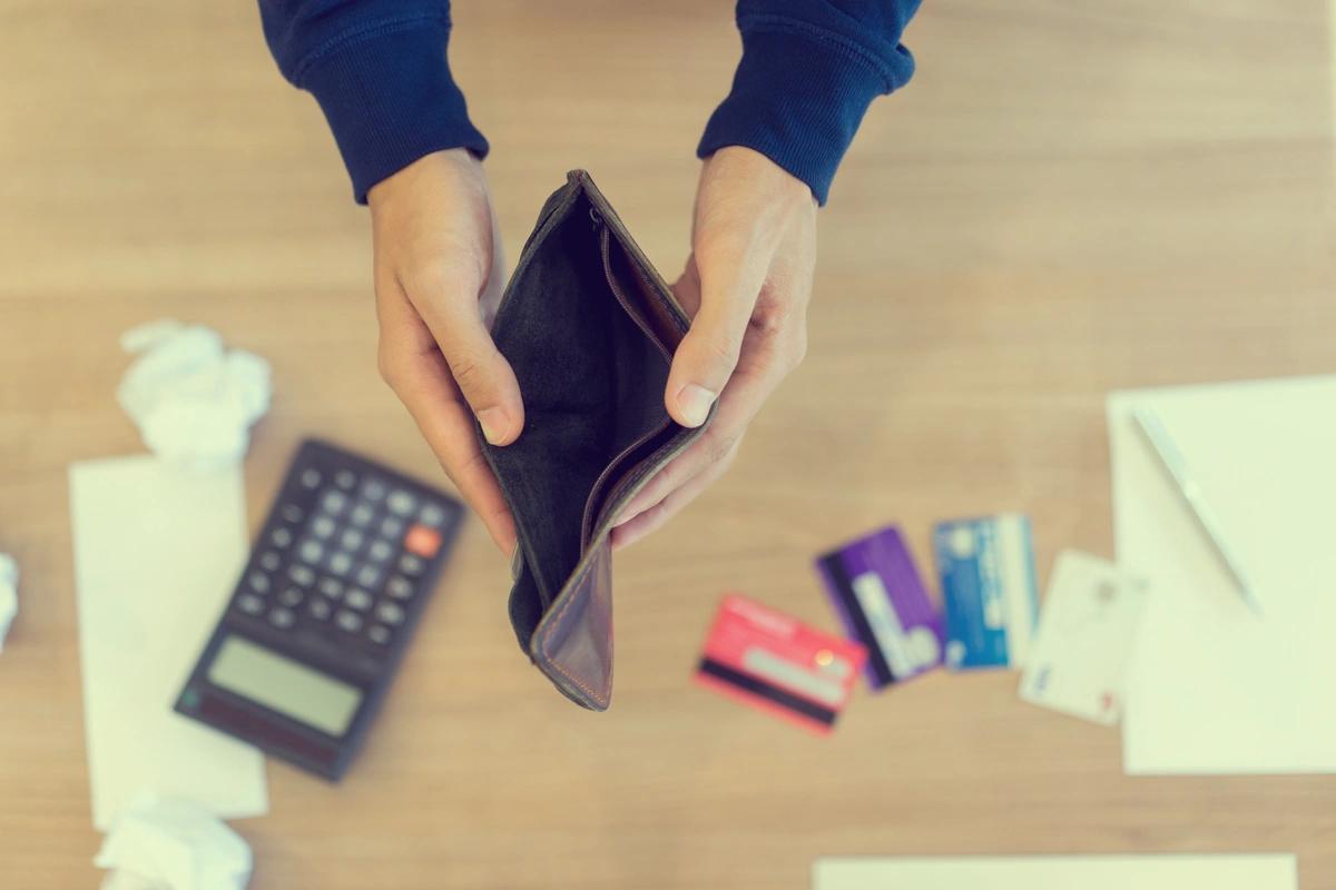 Close up of man holding open empty wallet over calculator, bank cards and screwed up bills