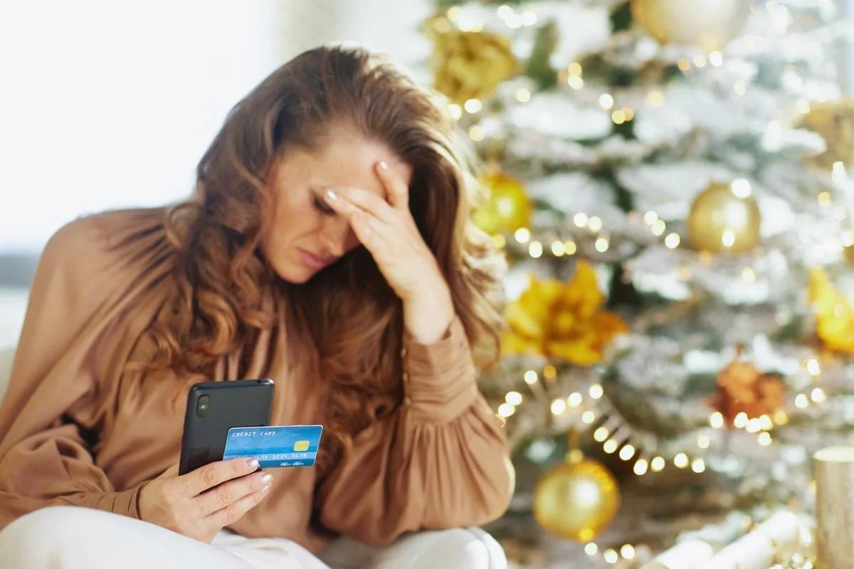 A woman in front of a Christmas tree with her head in her hands as she goes through her credit card bill