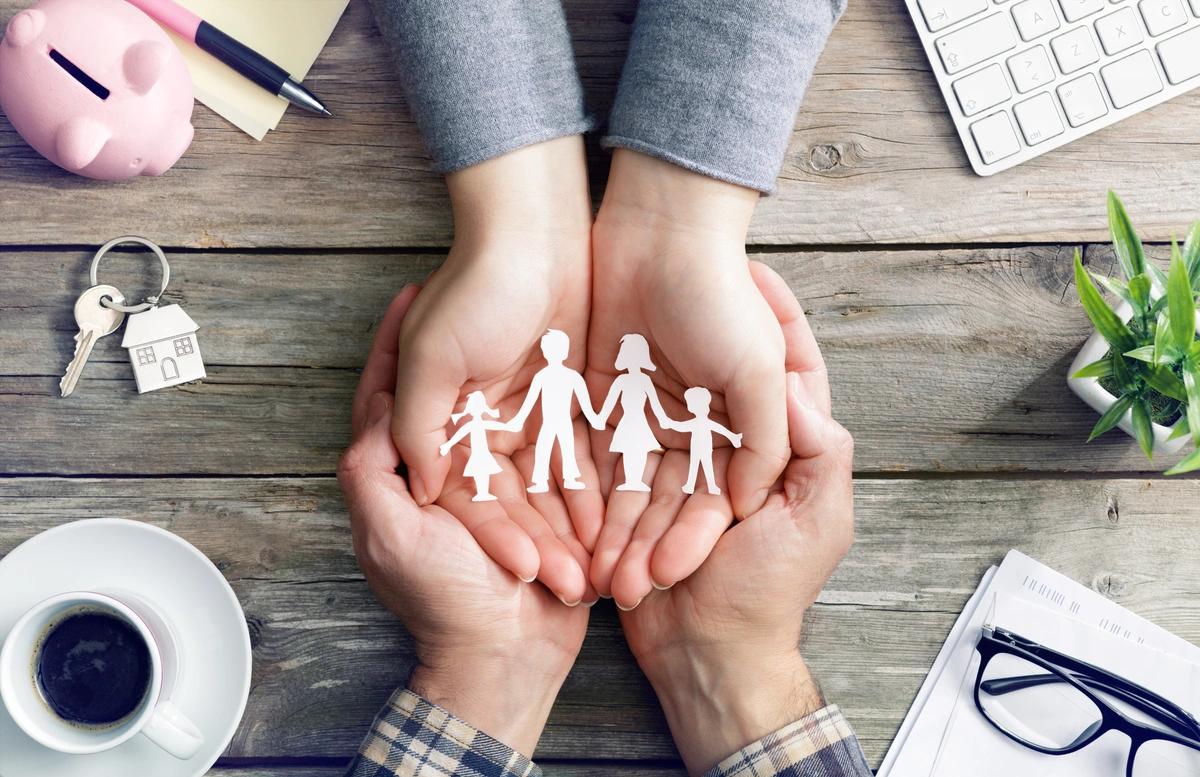 Two pairs of hands cradle a paper cutout of a family