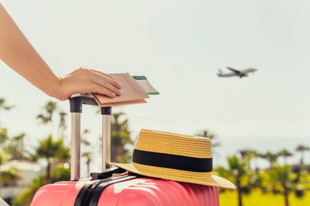 Image of a hand on top of a suitcase with a passport in the hand and a hat on top of the case