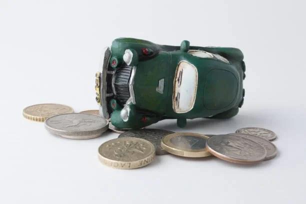 Image of a green toy car on its side on top of pound coins. 10 easy ways to save hundreds on motoring. Slash costs with simple fixes that keep your car - and your cash - running smoothly.