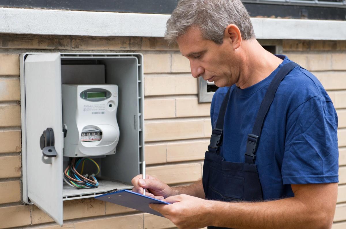 An electrician standing in front of an electricity meter with a clipboard