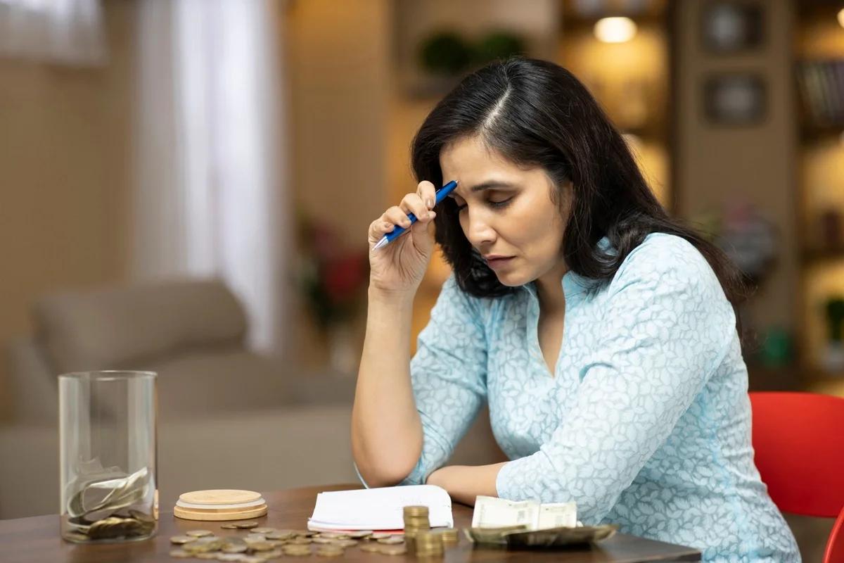 A worried woman sits at a desk going through her finances