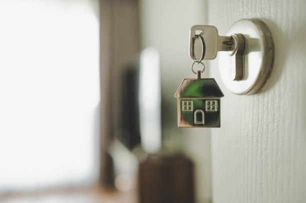 Image of a key in a door and the key ring has a little house on it