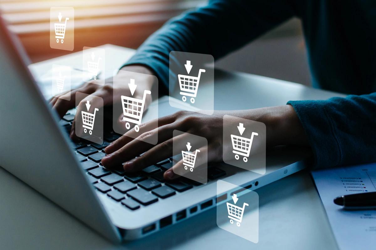 A close-up of a man's hands on a keyboard with shopping trolley symbols floating above the keys