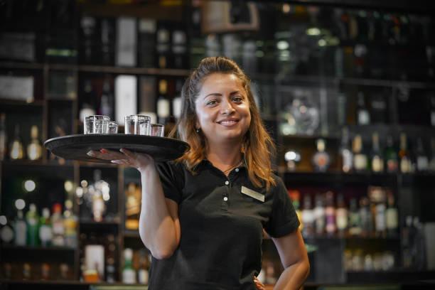 Image of a woman carrying a tray of drinks. Millions of workers to get pay boost from changes to tipping legislation