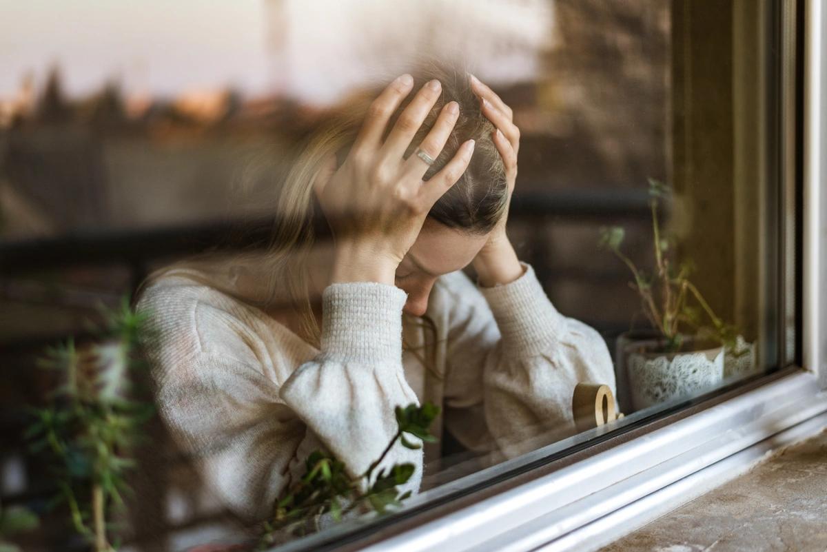 A woman standing by the window with her head in her hands