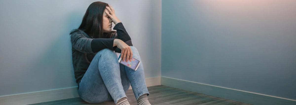 A worried woman sits on the floor considering whether to seek help with financial abuse