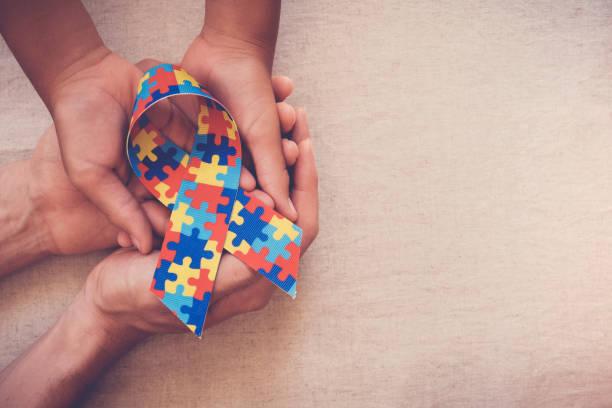 A photo of four hands holding an autism awareness ribbon with puzzle pieces on it