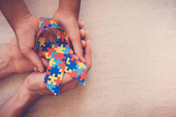 hand holding a ribbon with the autism awareness logo