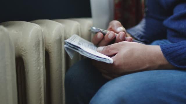 Image of a man huddled over a radiator with a mobile phone in his hand and an energy bill in the other