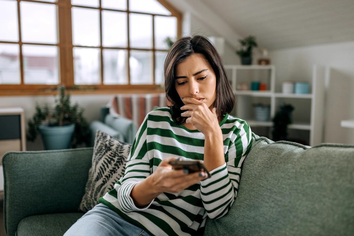 A woman looking at her phone realises she's been conned into transferring money by a conman