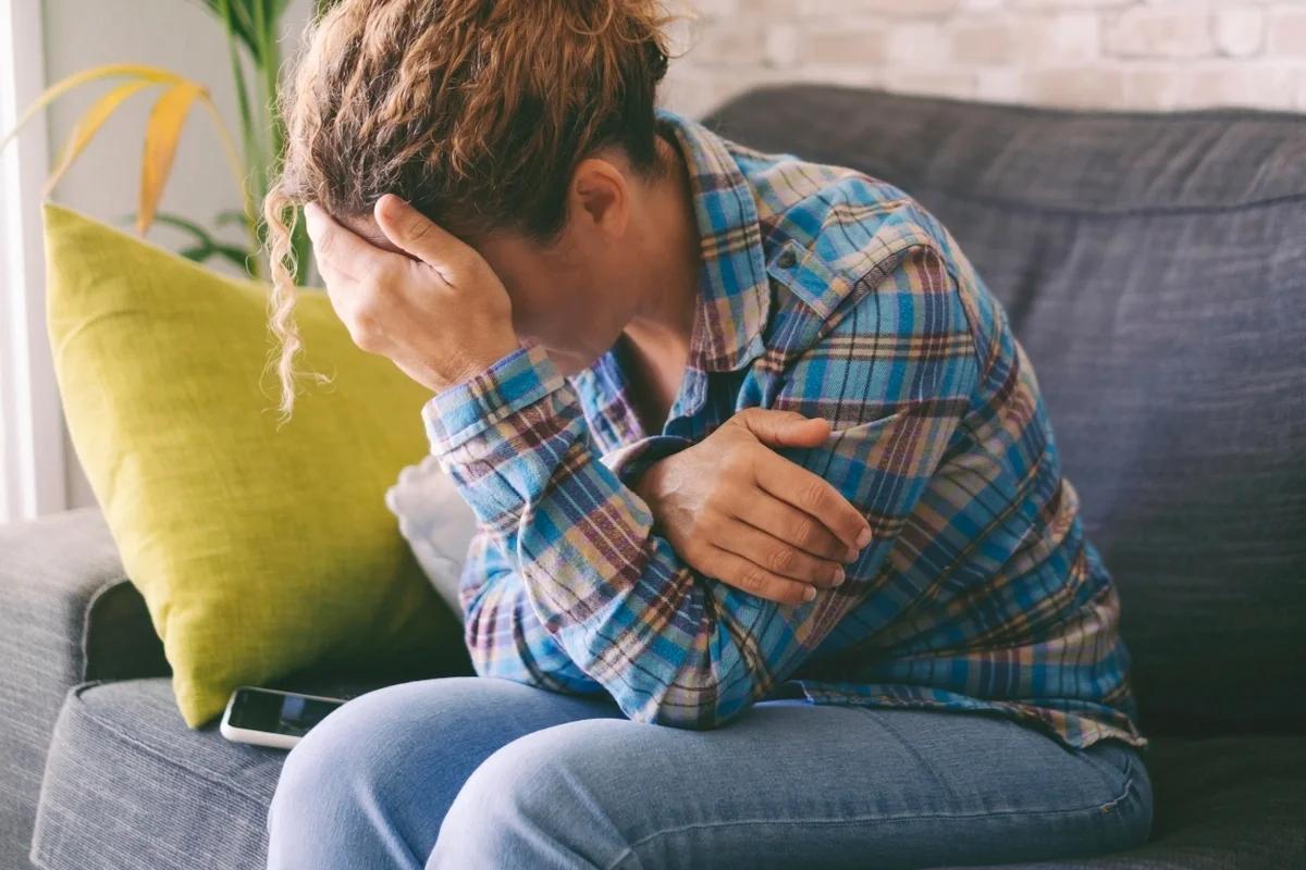 A woman sits on a sofa with her head in her hands