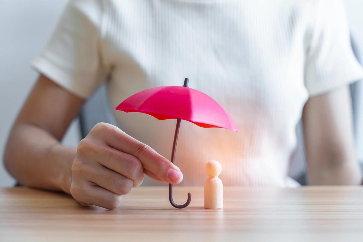A close up of a woman's hand holding a tiny red umbrella over  a small wooden figure