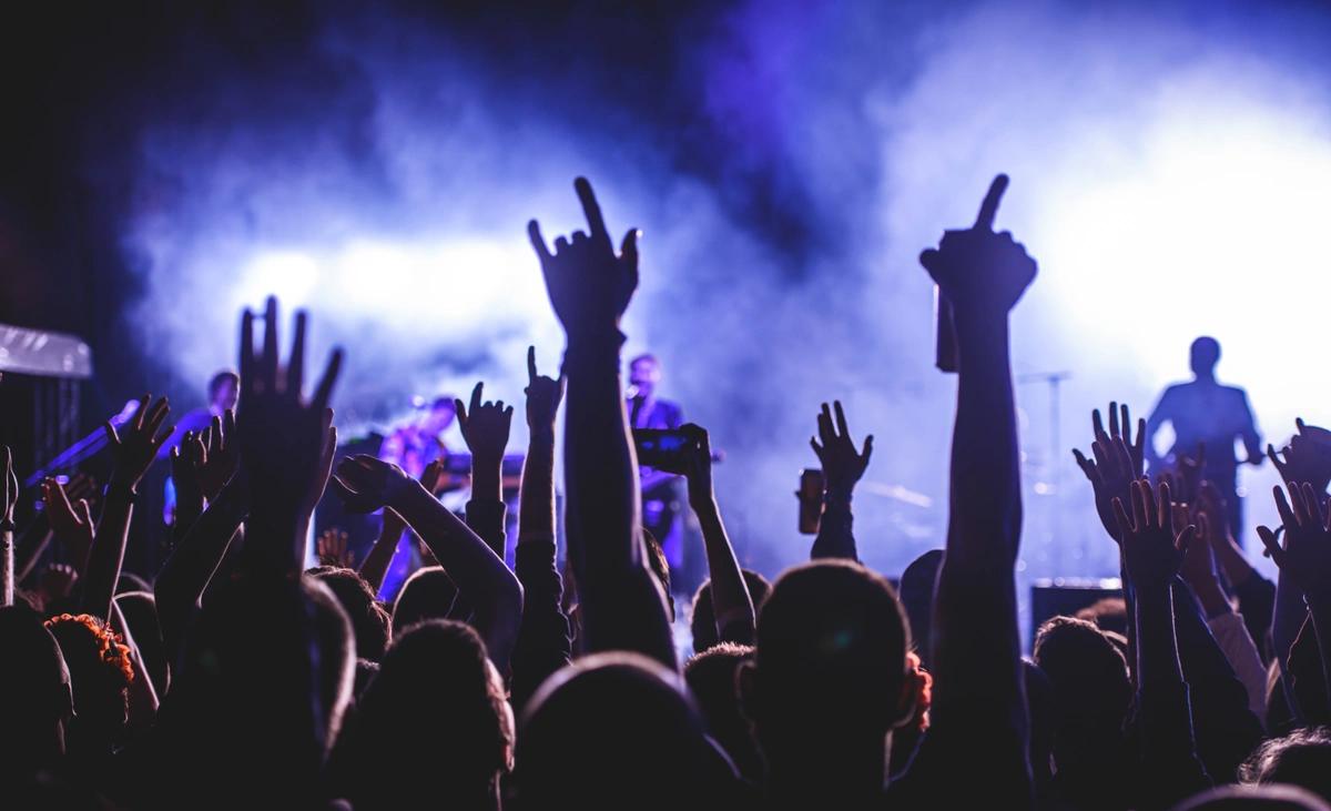 A crowd of people with their hands in the air as they watch a live band play on stage