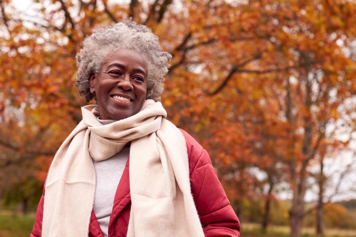 Head and shoulders shot of female pensioner on autumn walk against a backdrop of trees