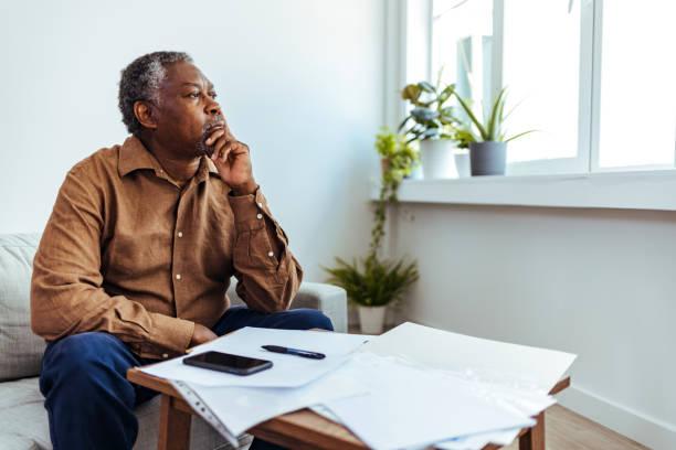 Image of a man looking pensively out the window with bills and a calculator set out in front of him