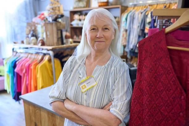 Image of a female pensioner working in a clothes shop with her name badge on. Retirees are going back to work because of cost of living pressures