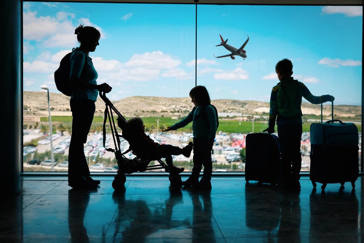 A mum and three children are silhouetted against an airport window with a plane flying past