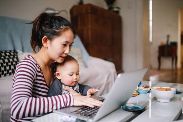 Image of a woman with a baby on her knee working on a laptop