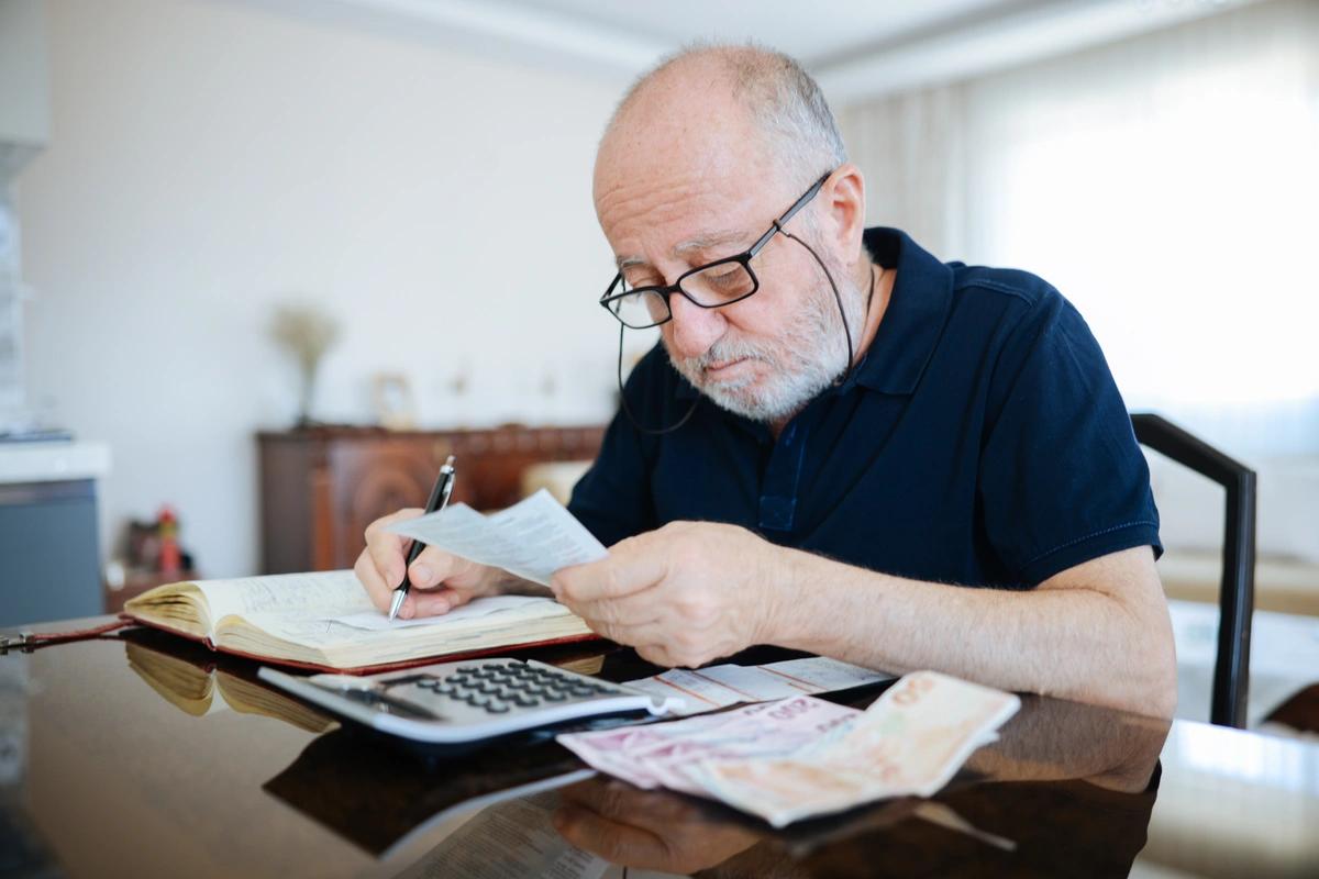 A pensioner sits at a desk going through his finances