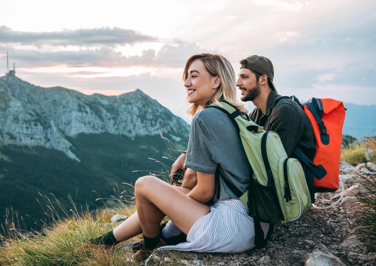 Two hikers sitting on top of a mountain smiling and taking in the view