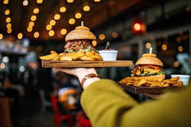 Image of a waiter or waitress carrying two burgers and chips on wooden platters