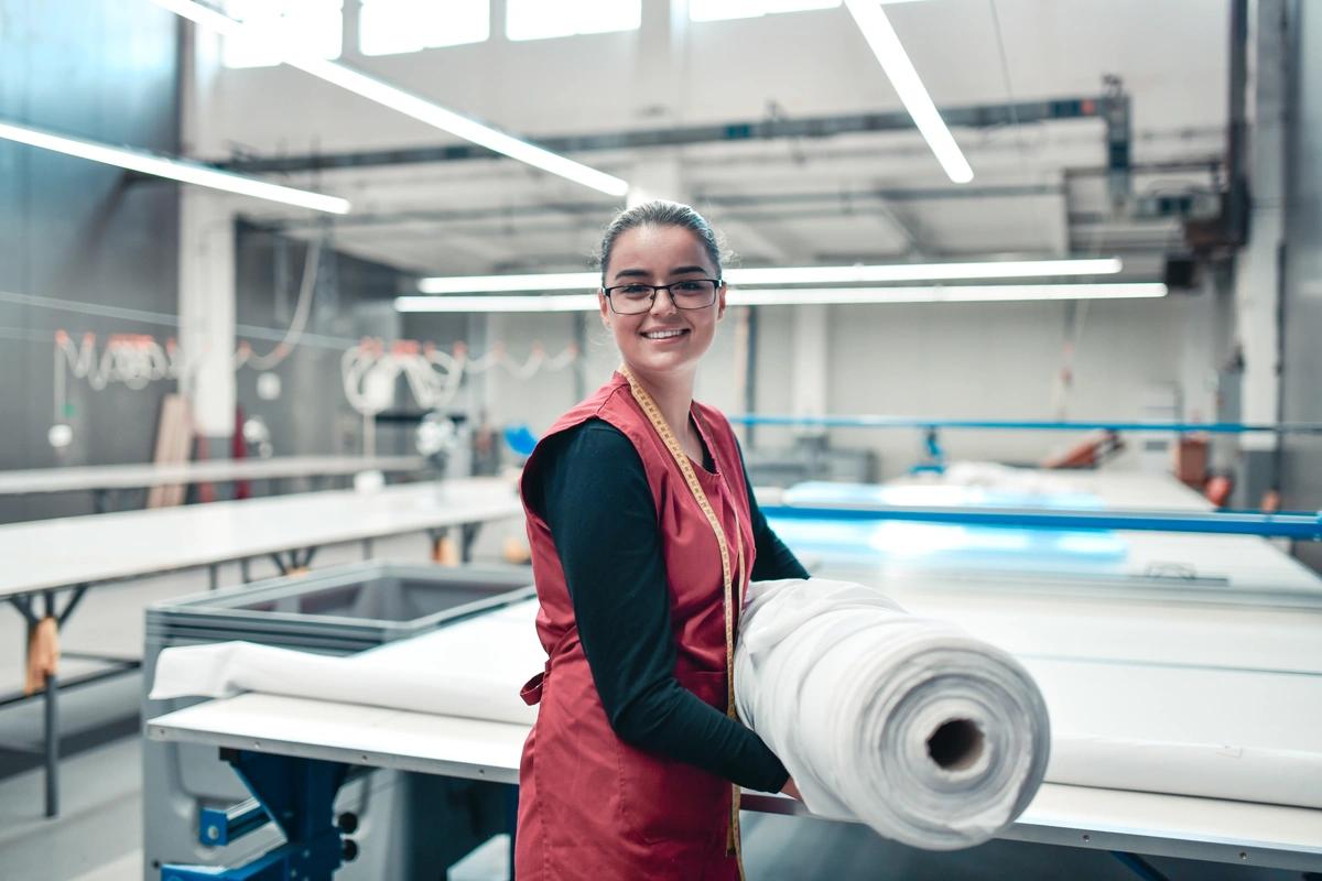 Smiling female textile worker carrying large roll of material