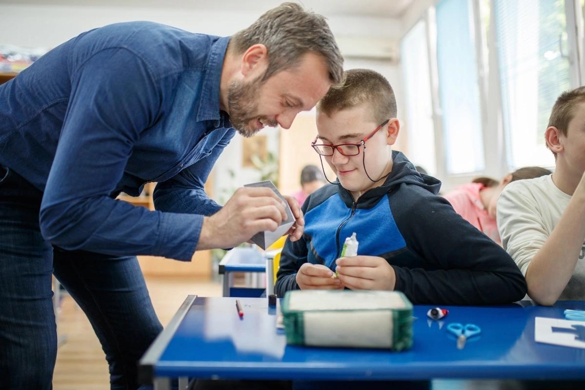 A teacher helps a boy with learning difficulties during a craft lesson