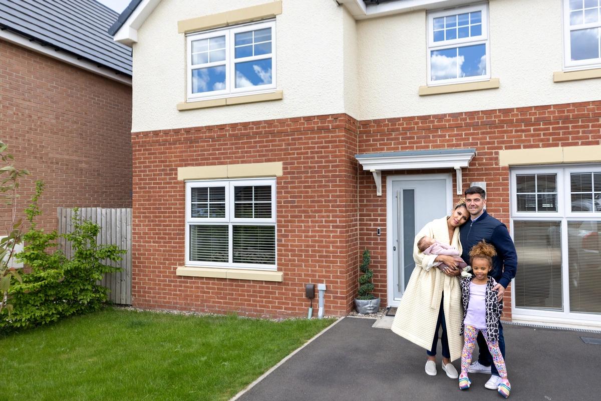 A family stand outside of a new build house, smiling