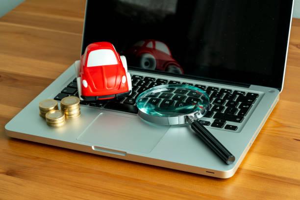 Image of a laptop open with a looking glass on top and also a toy car and a pile of coins