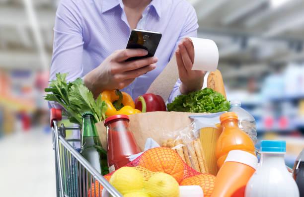 Image of a woman with a trolly of food and a calculator adding up the price