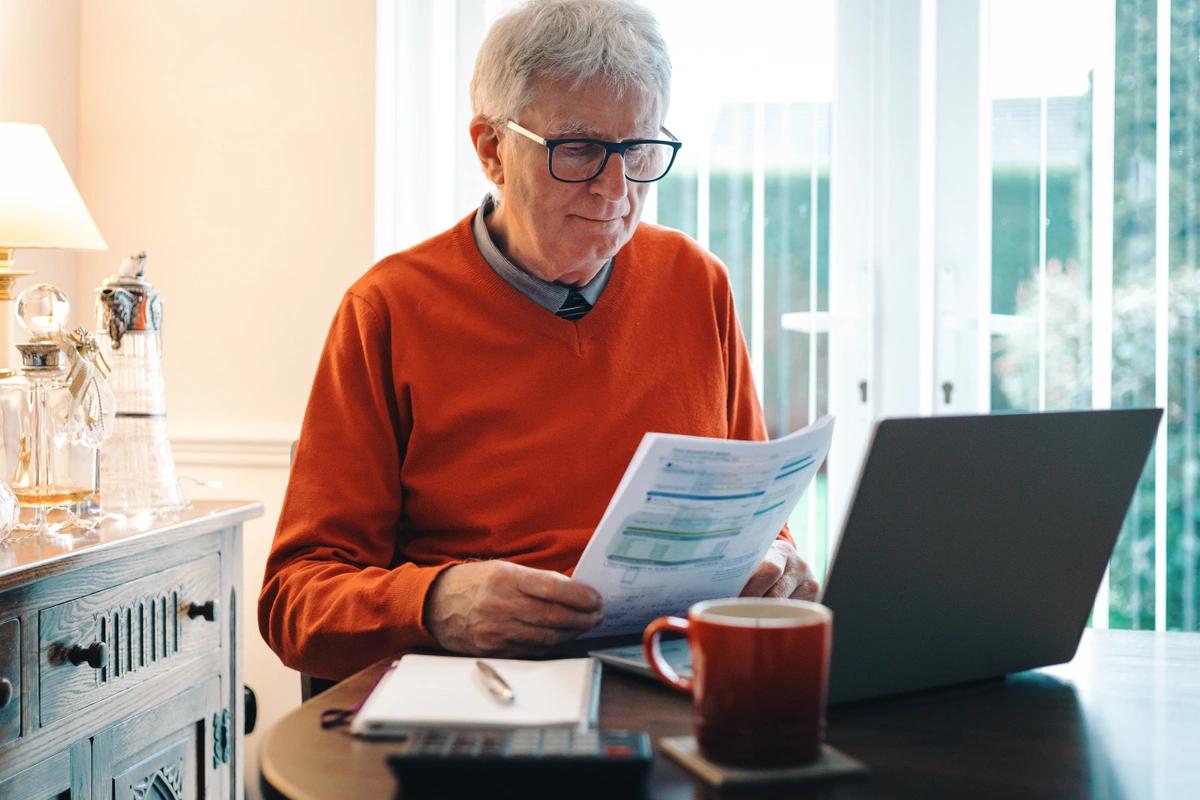 an older man holding documents near his laptop