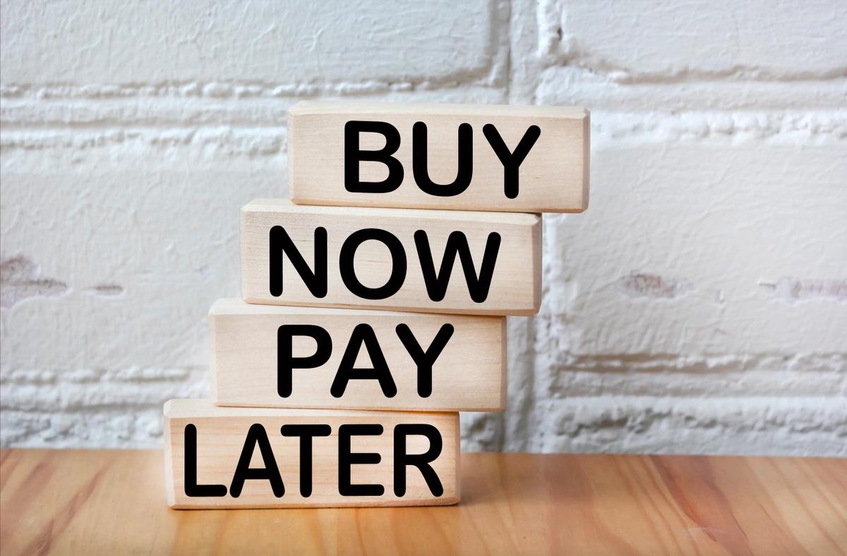 Wooden blocks against a whitewashed brick wall spelling out buy-now-pay-later