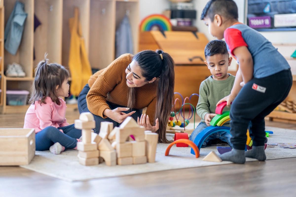 Three young children on a playmat with a childminder at nursery