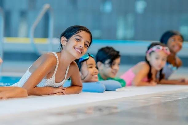 Image of several kids holding onto the side of a swimming pool. 11 free things for kids this summer that many parents don't realise are available. Lots of lesser known ways to keep kids busy for free or cheaply this summer