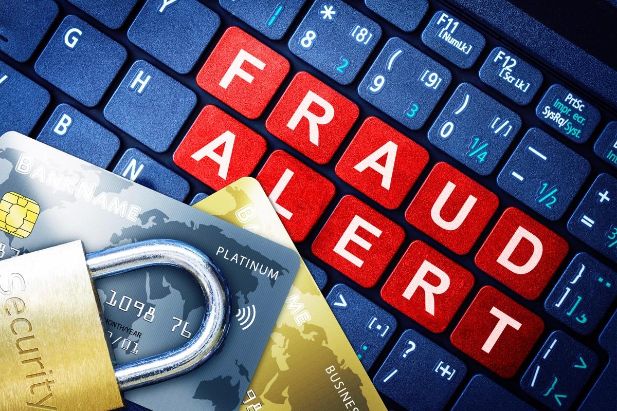 A computer keyboard with red keys spelling out "fraud alert", a padlock and some bank cards